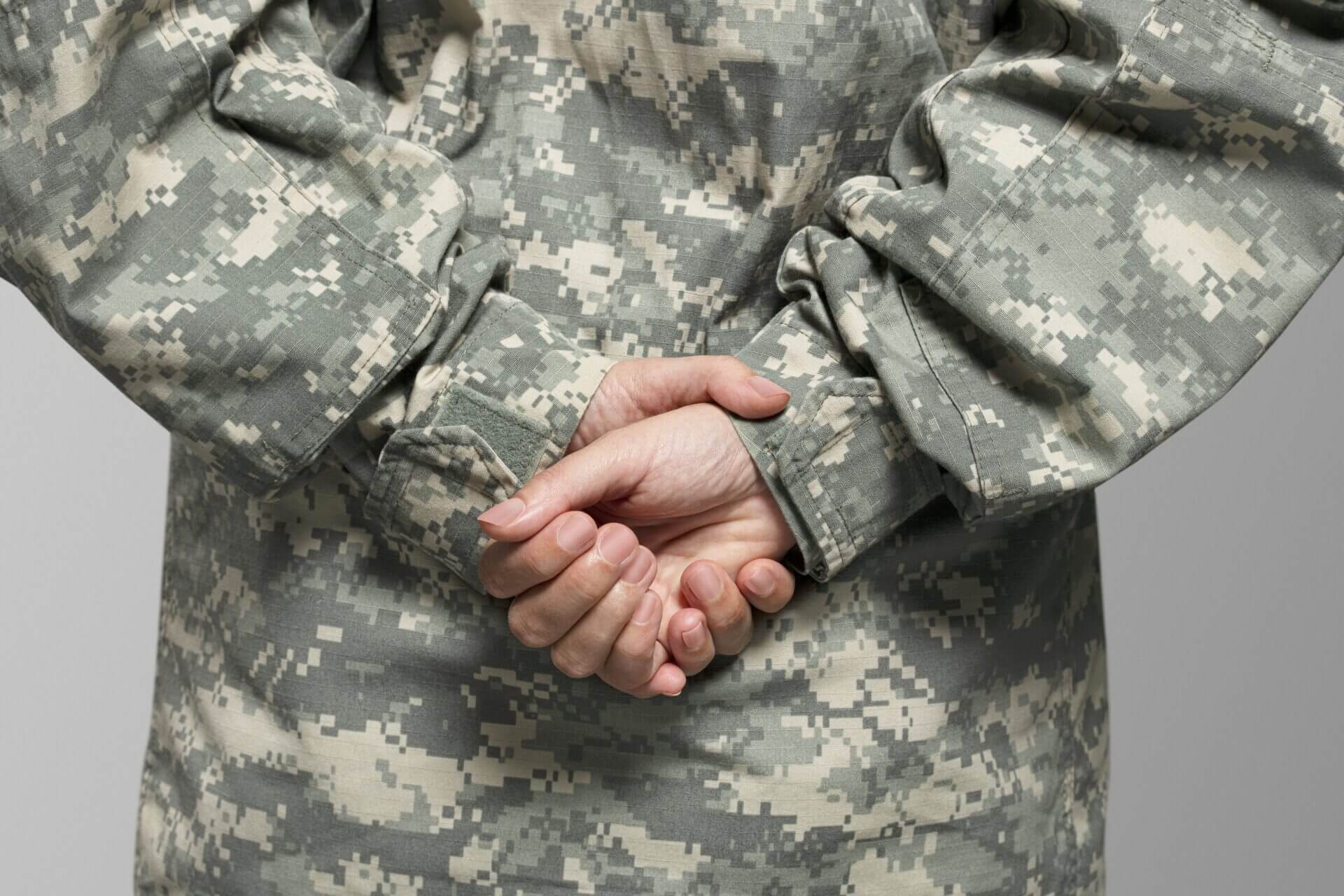 A person in fatigues is holding their hands together.