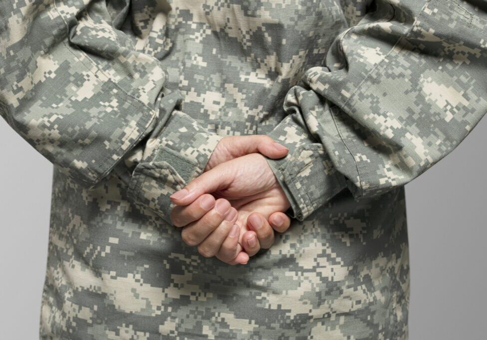 A person in fatigues is holding their hands together.